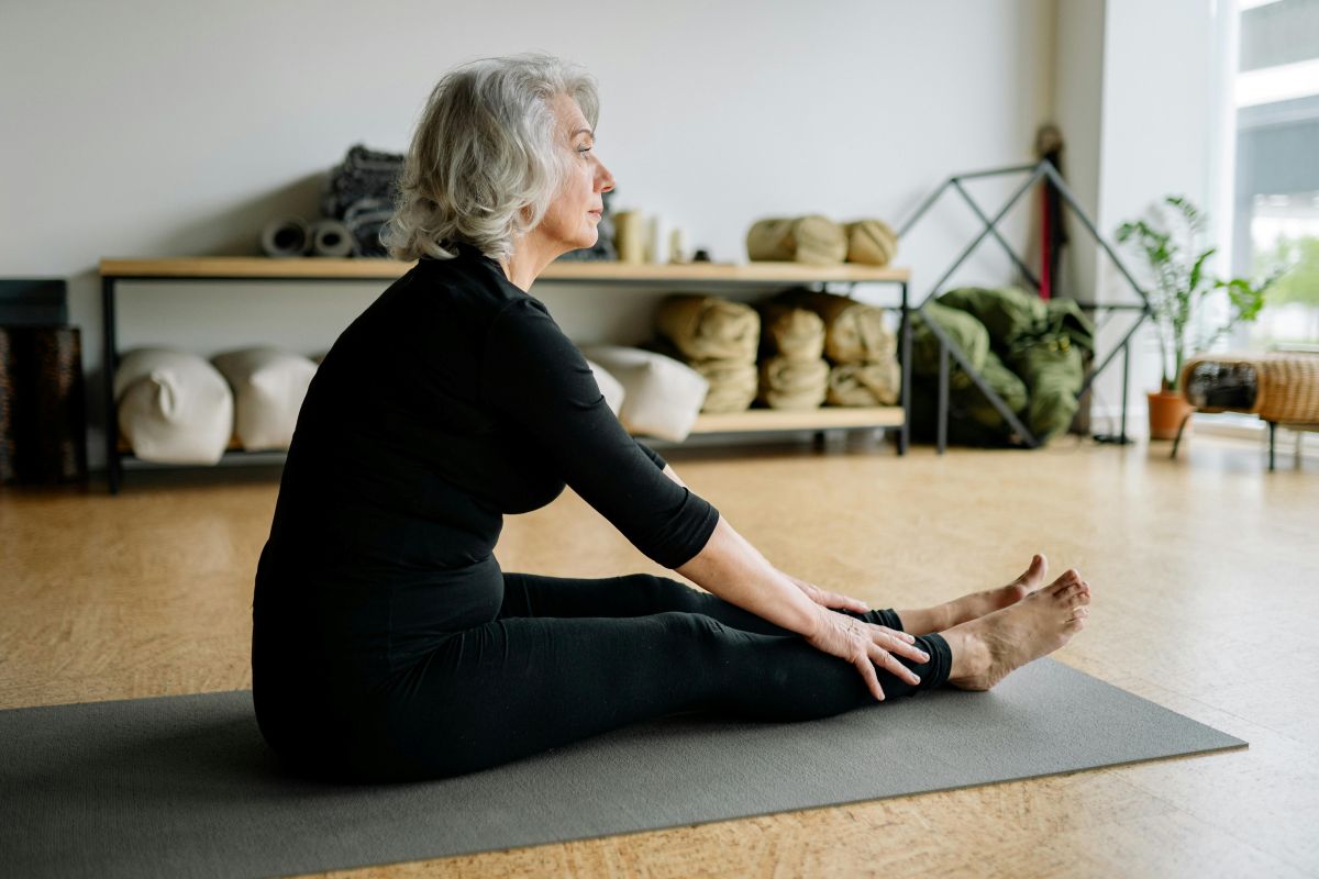 Uma mulher mais velha praticando yoga em um tapete de exercício, ilustrando como o exercício físico e uma dieta rica em vitamina D e cálcio são essenciais para manter a saúde óssea.